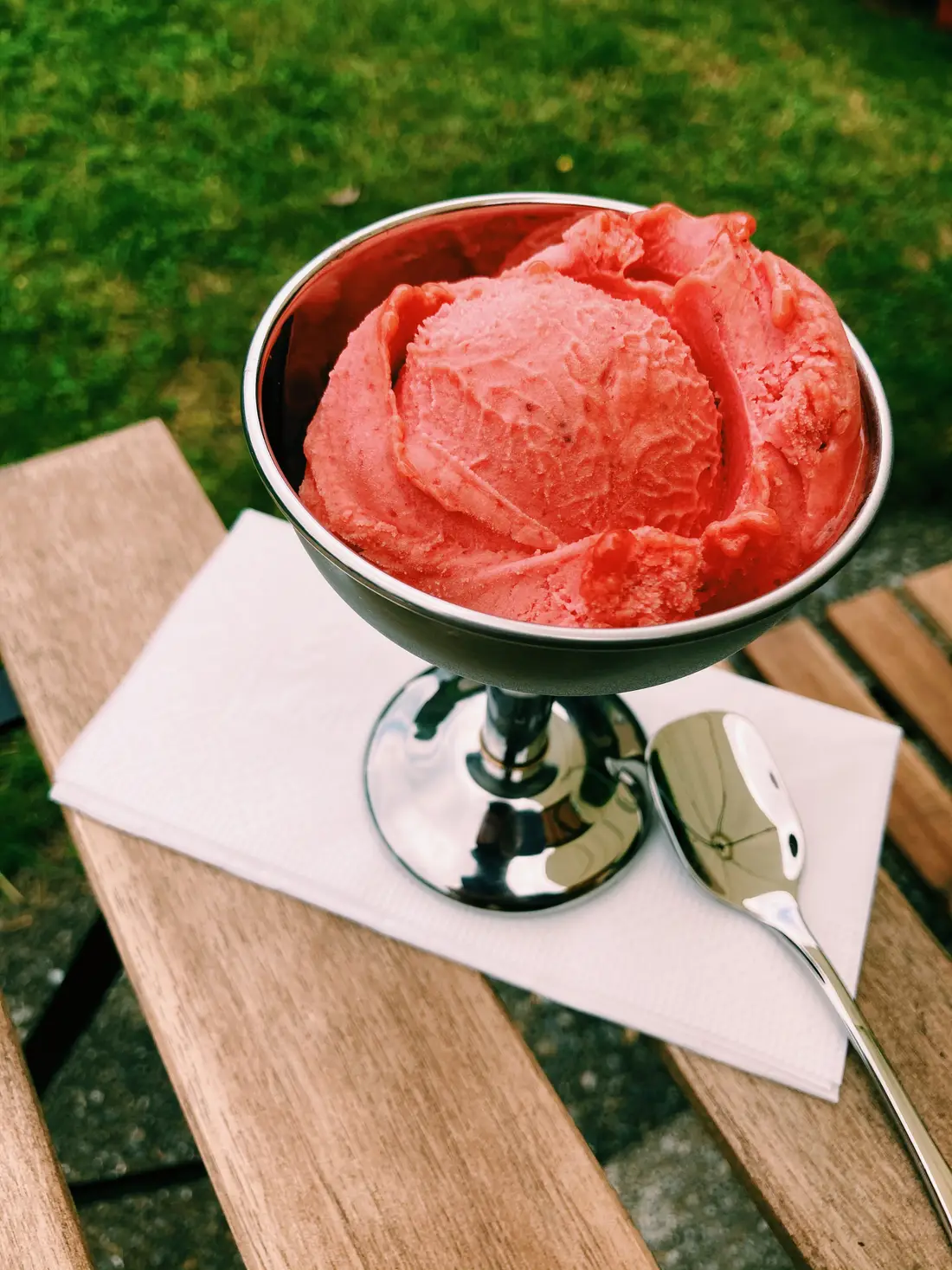 Erdbeer-Gelato im silbernen Coppa-Becher auf einer Serviette, auf einem Holztisch im Garten