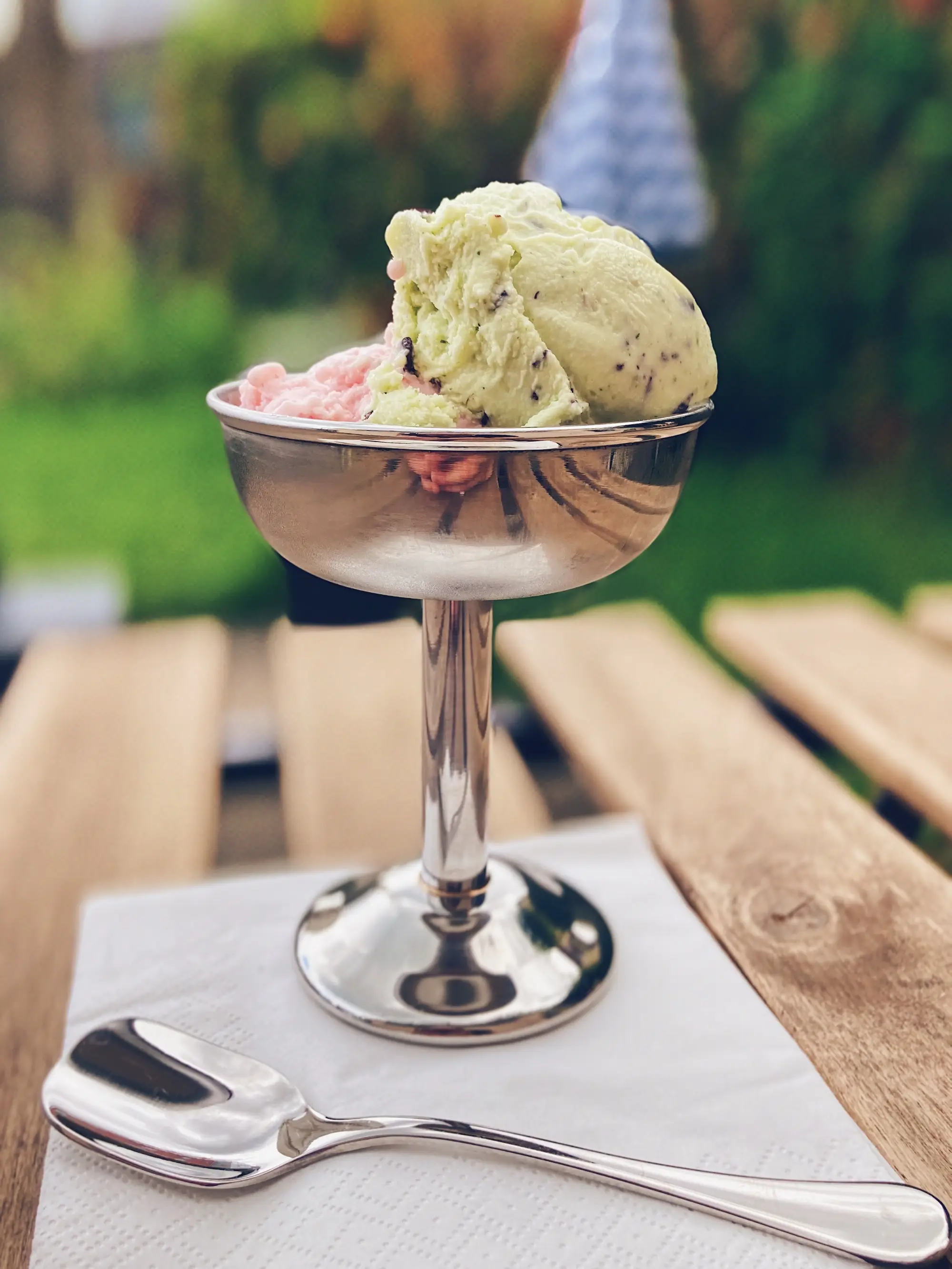 Zwei Kugeln Gelato im silbernen Coppa-Becher auf einem Holztisch im Garten